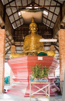 Golden Buddha image under a simple roof at a temple in Myeik, Myanmar.