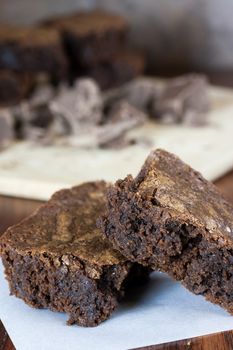 Chocolate brownies on a piece of parchment paper and chocolate chuncks on a cutting board in background.