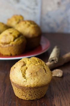 Pumpkin muffins on a wooden counter with cinnamon and nutmeg in the background.