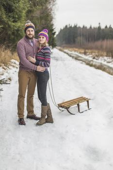 Happy couple pulling sled in winter snowy wood