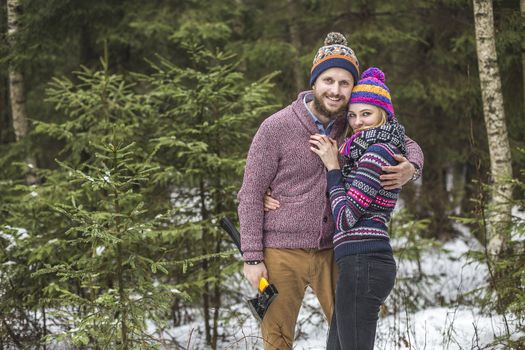 Lovers have a walk in the winter wood with an axe to cut a fir tree