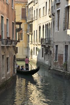 Gondola with tourists boating in a narrow canal in Venice, Italy