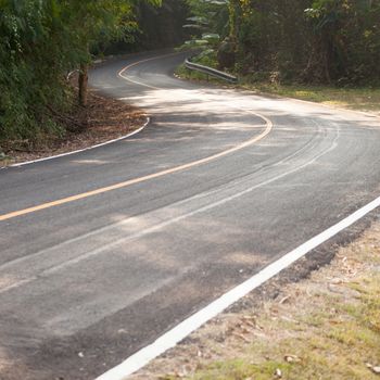 Curvy road down the hill. Road curving down from the mountain. There are more trees on either side of the road.