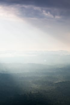 Sunlight shines through the clouds into the mountains and forests. Mist-covered mountains and trees.