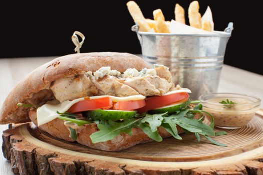 Healthy wheat sandwich burger with BBQ  grilled chicken steak, cheese, tomato, rocket salad, cucumber, fried potato and mustard sauce  served for eating on wooden board