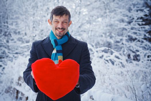 Man holding red heart in his hands in winter forest