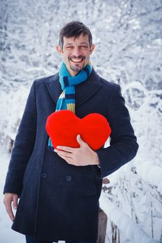 Man holding red heart in his hands in winter forest