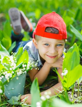 Cute little boy with lilies of the valley in forest on spring day