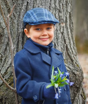 Cute little boy in forest with primroses flowers on spring day