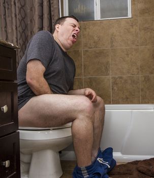 Male on a toilet in the bathroom making a funny face from masterbating