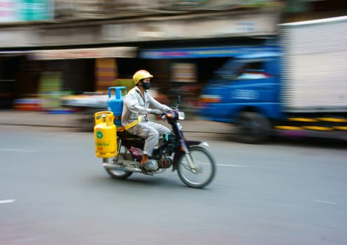 HO CHI MINH CITY, VIET NAM- MAR 30: Asian delivery man moving on street, Vietnamese male transport gas tank, guy in worker uniform, ride motorbike on Saigon road, Vietnam, Mar 30, 2013