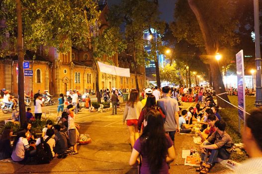 HO CHI MINH CITY, VIET NAM- DEC 24: Crowded atmosphere at Duc Ba Cathedral at Xmas night, under yellow lamp, young people sit on pavement, enjoy bet cafe, is youth lifestyle, Vietnam, Dec 24, 2014