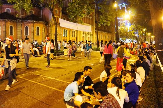 HO CHI MINH CITY, VIET NAM- DEC 24: Crowded atmosphere at Duc Ba Cathedral at Xmas night, under yellow lamp, young people sit on pavement, enjoy bet cafe, is youth lifestyle, Vietnam, Dec 24, 2014