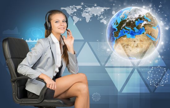 Businesswoman in headset, sitting on office chair, her hand on microphone, looking at camera, smiling. Globe, world map, communication network and other virtual elements as backdrop. Element of this image furnished by NASA