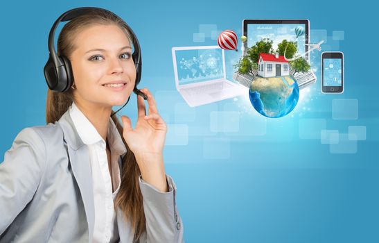 Businesswoman in headset, her hand on microphone, looking at camera, smiling. Beside are Globe with small house, high-rise buildings, trees, airplane and balloons, surrounded by computers and smartphone, on light blue background