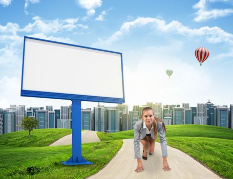 Businesswoman standing in running start pose on the road among green hills, against distant cityscape behind her back and balloons in the sky. Blank billboard beside. Looking at camera. Business concept