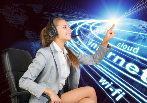 Businesswoman in headset sitting on office chair, touching spot of light with rays around, smiling. Beside is Globe surrounded by light streams of communication. World map composed of digits as backdrop. Element of this image furnished by NASA