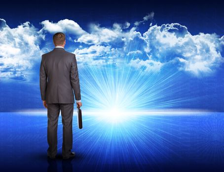 Businessman with briefcase standing against digitally generated spacy blue landscape with rising sun and cloudy sky 