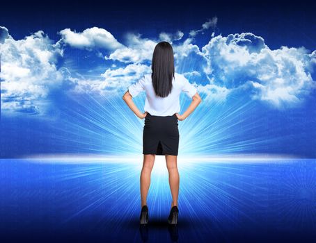 Businesswoman standing akimbo against digitally generated spacy blue landscape with rising sun and cloudy sky