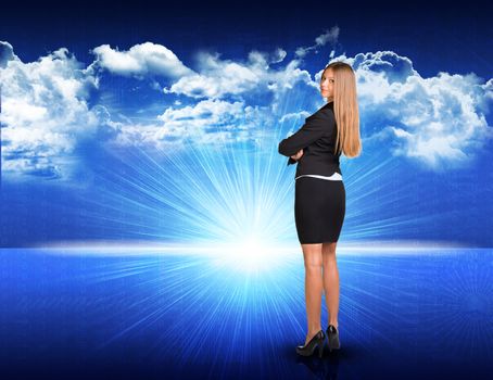 Businesswoman standing against digitally generated spacy blue landscape with rising sun and cloudy sky, looking back over her shoulder