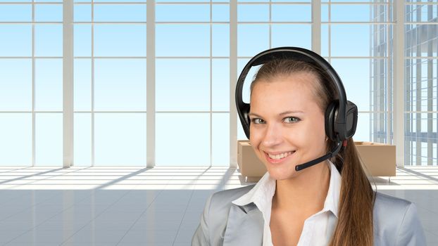 Businesswoman in headset, in vast white interior with transparent wall, looking at camera, smiling