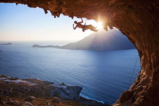 Male rock climber climbing in cave with beautiful view in background