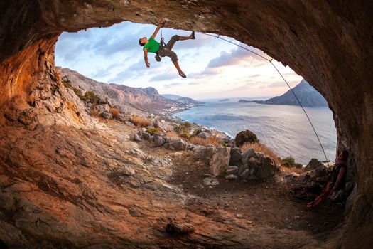Male rock climber climbing along a roof in a cave at sunset. Kalymnos Island, Greece