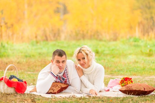 man and woman relaxing comfortably on the plaid in the park