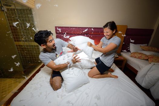 happy loving asian couple having a pillow fight in bed at night