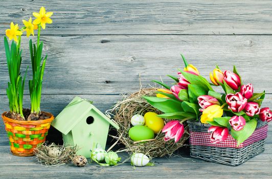 easter decoration with eggs, birdhouse and tulips. wooden background