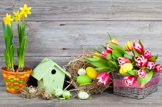 easter decoration with eggs, birdhouse and tulips. wooden background