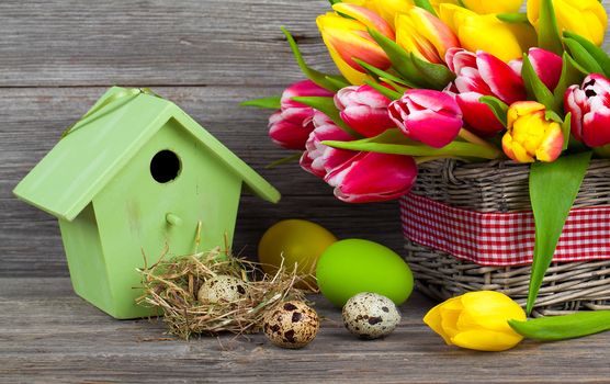 easter decoration with eggs, birdhouse and tulips. wooden background