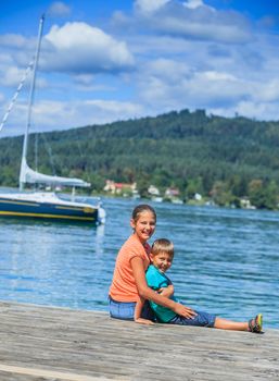 Summer vacation  at the lake - two happy kids resting on the pier and watching on the yacht