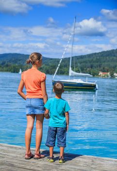 Summer vacation  at the lake - two happy kids walking on the pier and watching on the yacht