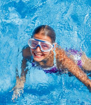 Cute happy young girl in goggles swimming and snorking in the swimming pool
