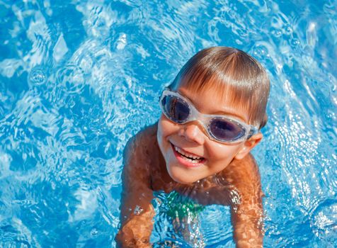 Cute happy little boy in goggles swimming and snorking in the swimming pool