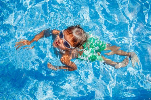 Cute happy little boy in goggles swimming and snorking in the swimming pool