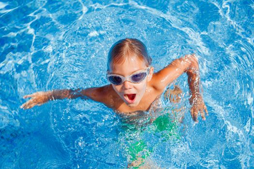 Cute happy little boy in goggles swimming and snorking in the swimming pool