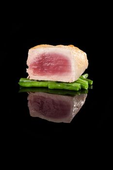 Grilled tuna steak on green beans isolated on black background. Healthy seafood eating.