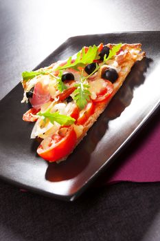 Delicious hot pizza piece triangle on black plate on table, minimal contemporary style. Fine dining.