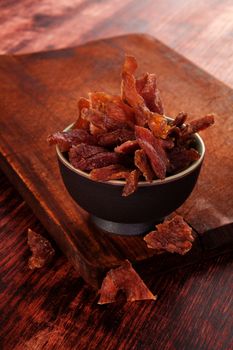 Beef jerky. Dried meat beef jerky on wooden chopping board on wooden background. Dry meat, rustic country style. Delicious meat eating. 