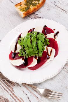 Beet with goat cheese and fresh salad on white vintage plate on white wooden textured background. Culinary delicious healthy eating.