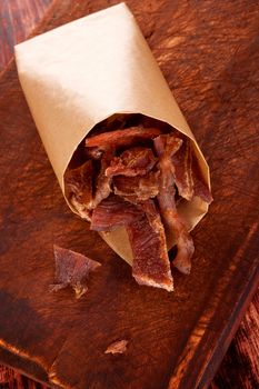 Beef jerky. Dry meat beef jerky on wooden chopping board on wooden background. Dry meat, rustic country style. Delicious meat eating. 