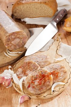 Head cheese on brown vintage cutting board with bread, garlic and onion. Traditional culinary eating. 