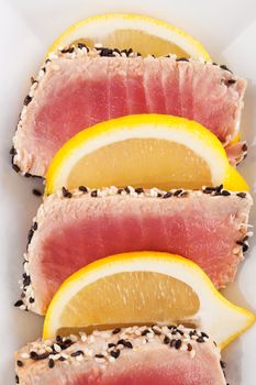 Tuna slices with sesame seeds and lemon slices on white plate. Culinary seafood, healthy eating. 