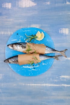 Two fresh mackerel fish on blue wooden kitchen board with lemon and rosemary on blue wooden textured background.
