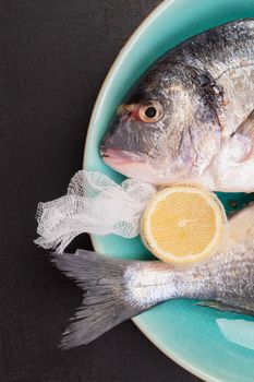 Delicious sea bream with lemon on turquoise plate on black background, top view. Mediterranean seafood background.