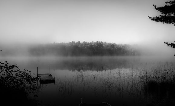 Uneven fog naturally frames the moment as cool September air mixes with the warmer northern Ontario lake water to create a misty morning.