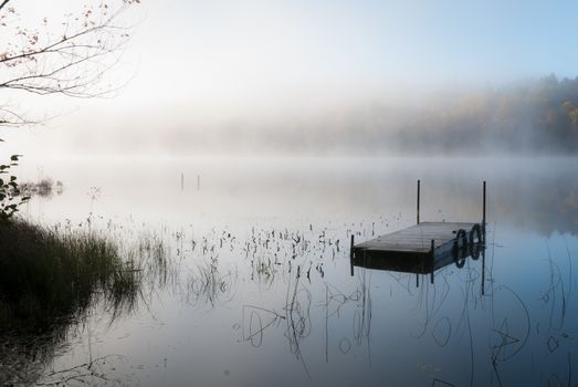 Early morning sunrise slowly burns off accumulated overnight fog over a Northern Ontario lake.