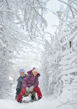 Boy And Girl at sledging Through Snowy in a fairytale landscape